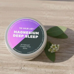 Magnesium Deep Sleep Balm tin on a wooden surface with leaves and a flower.