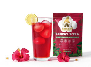 Glass of hibiscus tea with ice and lemon slice next to tea bag packaging.